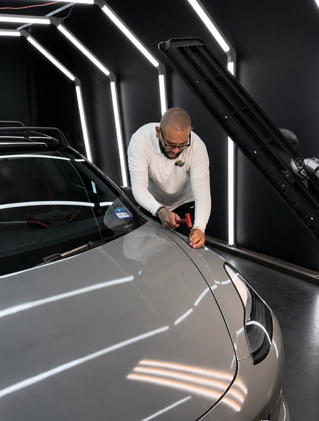 Lone Star PDR master technician performing paintless dent repair on a hood under calibrated light lines